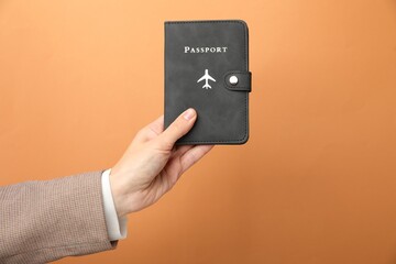 Woman holding passport in bright cover on orange background, closeup