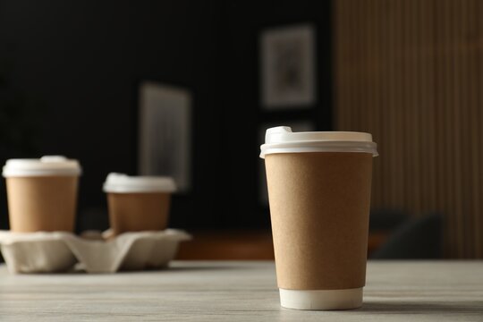 Paper cup on light wooden table in cafe, closeup. Mockup for design