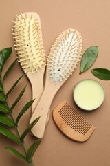 Wooden hair brushes, comb, wax and green branch on dark beige background, flat lay