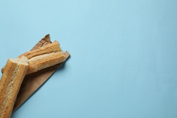 Paper bag and fresh baguette on light blue background, top view. Space for text