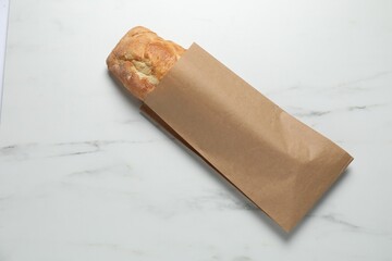 Paper bag with fresh baguette on white marble table, top view