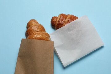 Paper bags with fresh croissants on light blue background, top view
