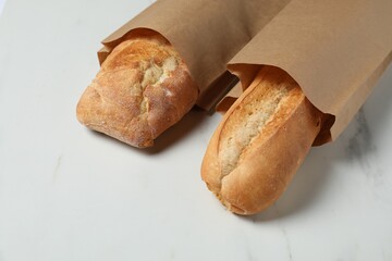 Paper bags with fresh baguettes on white marble table, closeup