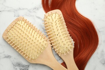 Wooden brushes and lock of hair on white marble table, flat lay