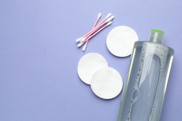Cotton pads, swabs and bottle of cosmetic product on violet background, flat lay. Space for text