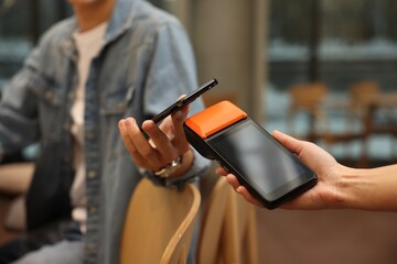 Man paying with smartphone via terminal in cafe, closeup