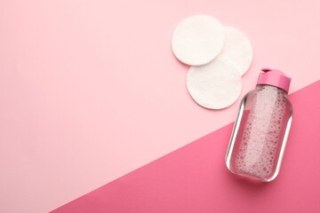 Clean cotton pads and micellar water on pink background, flat lay. Space for text