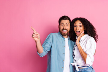 Excited couple pointing and smiling against a vibrant pink background