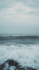 Fototapeta premium Ocean waves crashing on the shore under a cloudy sky