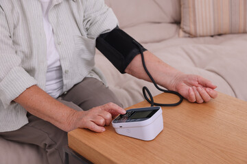 Senior woman measuring blood pressure at wooden table indoors, closeup