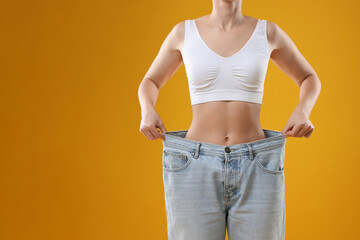 Weight loss. Woman wearing big jeans on yellow background, closeup. Space for text