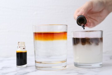 Iodine starch test. Woman dripping aqueous iodine into glass of water containing starch at white marble table, closeup