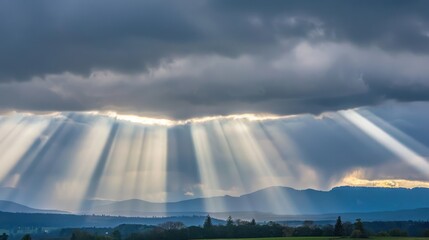 Dramatic sun rays breaking through dark clouds over mountains.