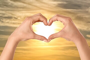 Fototapeta premium Female hands making heart against cloudy sky at sunset