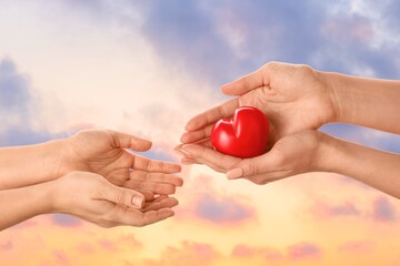 Hands with red heart against cloudy sky