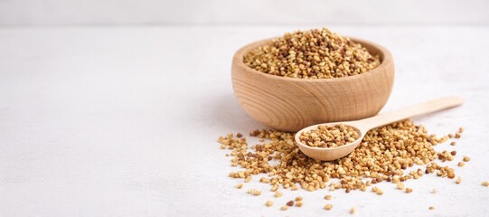 Wooden bowl and spoon with raw buckwheat grains on light background with space for text