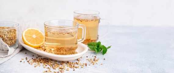 Glass cups of buckwheat tea, mint and lemon on light background with space for text