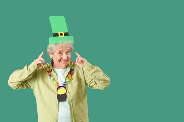 Happy senior woman pointing at paper leprechaun hat for St. Patrick's Day celebration on green...