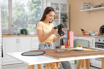 Young female photographer taking picture of dessert in kitchen