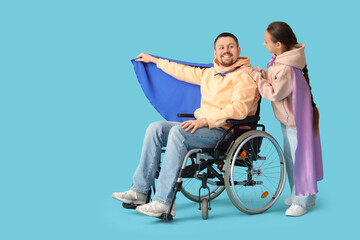 Little girl and her father in wheelchair with superhero capes on blue background