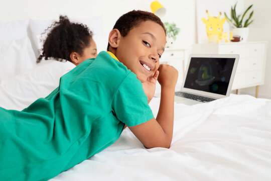 Cute happy African-American children watching cartoons on laptop in bedroom at home - Powered by Adobe