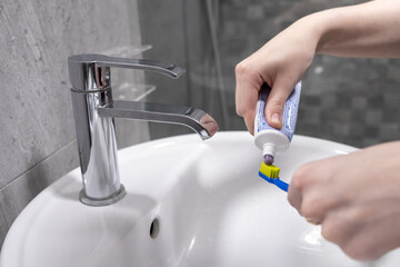 Squeezing toothpaste onto a toothbrush over a white sink in a bathroom hygiene routine