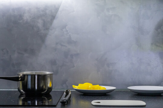 Modern kitchen countertop with steaming pot, sliced yellow bell pepper on plates, and cutting board under soft light - Powered by Adobe