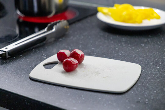 Fresh radishes on a cutting board with kitchen tongs and yellow bell peppers in the background