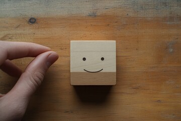 Hand Holding a Wooden Block with a Smiling Face on a Rustic Table, Symbolizing Joy and Playfulness in Minimalistic Design Aesthetic
