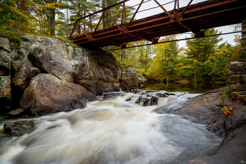 Long exposure waterfalls under a steel, iron and wood bridge, surrounded by autumn fall colors.