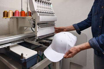 Woman with blank baseball cap for print using embroidery machine indoors, closeup