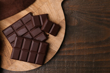 Pieces of delicious dark chocolate bar on wooden table, top view. Space for text