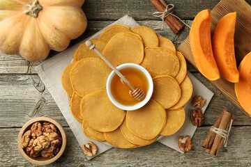Tasty pumpkin pancakes, honey, walnuts and cinnamon on wooden table, flat lay