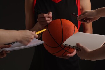 Sportsman signing autograph on basketball ball against black background, closeup