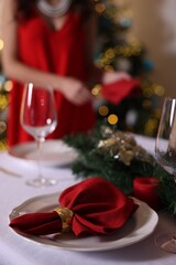 Woman setting table for Christmas dinner at home, focus on plate, napkin and decor