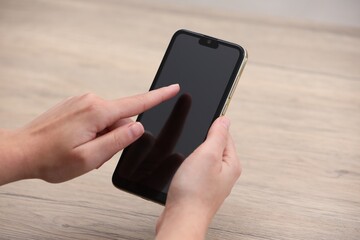 Woman using smartphone with blank screen at wooden table, closeup