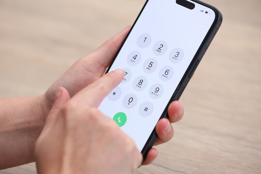 Woman dialing number on smartphone at wooden table, closeup