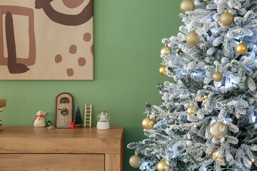 Christmas tree and decorations on chest of drawers near green wall in room