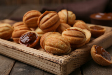 Cutting board of sweet walnut shaped cookies with boiled condensed milk on wooden background, closeup