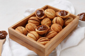 Wooden box of sweet walnut shaped cookies with boiled condensed milk on white background, closeup