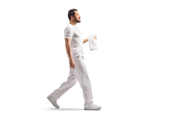Full length profile shot of a male massage therapist holding a towel and walking