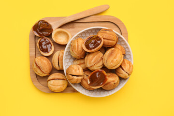 Bowl and wooden board of sweet walnut shaped cookies with boiled condensed milk on yellow background