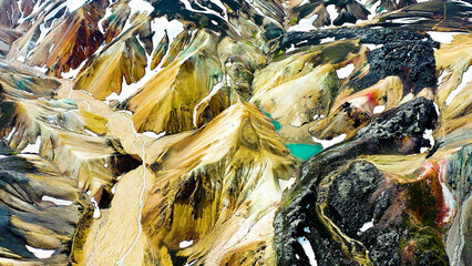 Aerial view of a snowed mountain range and colored mountains in the highlands of Landmannalaugar, Iceland.