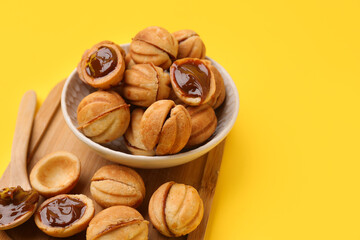 Bowl and wooden board of sweet walnut shaped cookies with boiled condensed milk on yellow background
