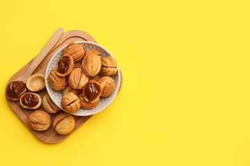 Bowl and wooden board of sweet walnut shaped cookies with boiled condensed milk on yellow background