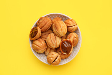 Bowl of sweet walnut shaped cookies with boiled condensed milk on yellow background