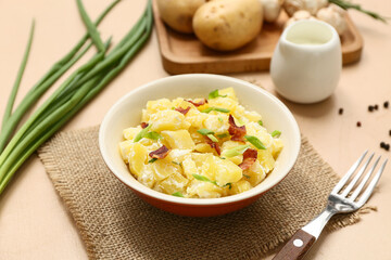 Bowl of tasty potato salad with bacon, green onion and peppercorns on beige background