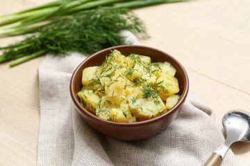 Bowl of tasty potato salad with dill and green onion on beige wooden background