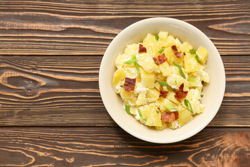 Bowl of tasty potato salad with green onion and bacon on wooden background