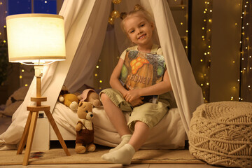 Cute little girl with book sitting in hut at home